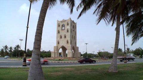 A static shot showing the Burj A'Nahdah on a roundabout in Salalah, Oman as cars circle round and date trees frame the shot