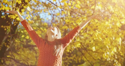 Happy woman throwing leaves in Autumn in slow motion, smiling. Slow Motion 120 fps. Joyful and excited young woman having fun throwing yellow leaves in the sunny fall park. 4k graded from RAW.