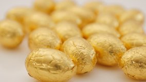Lot of golden foil wrapped  Easter chocolate eggs on white background  4K 3840X2160 30fps UHD footage - Traditional Easter gold eggs on white surface 4K 2160p UltraHD video