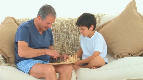 A Caucasian boy playing chess with his grandfather on the sofa