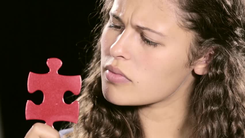Puzzled young woman frowns at single red jigsaw puzzle piece, tapping her chin as she thinks, then looking at the camera, seeking an answer to her unsolved problem Royalty-Free Stock Footage #11161418