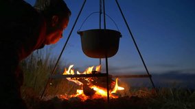 4 in 1 video! The man near cauldron with food on the fire by picturesque landscape backround. Shot with Red Cinema Camera