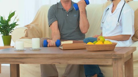 A Caucasian patient using dumbbells next to his nurse