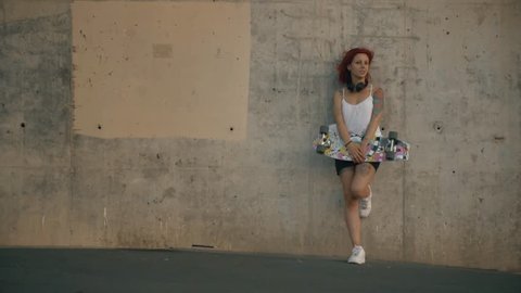 Tattooed red head woman stands in a concrete wall with his skateboard स्टॉक वीडियो