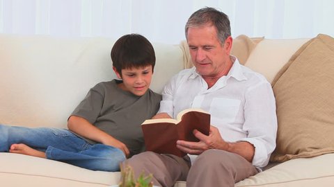 Casual man reading a book with his grandson on the sofa