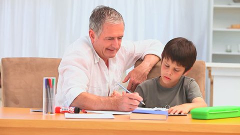 A grandfather helping his grandson to do his homework in the living room