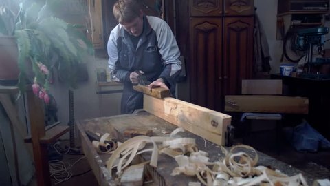 Hard working man is working in his shop on the plank of wood on the bench, footage is taken in slow motion.