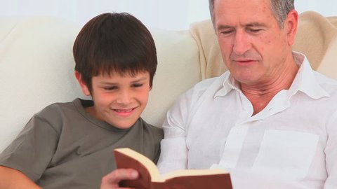 A lovely child listening to his grandfather reading a book
