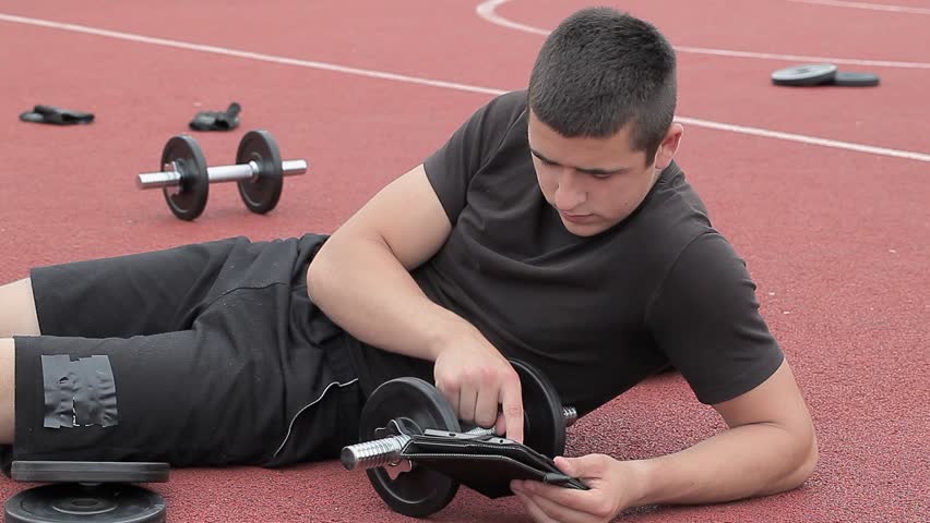 Teenager using tablet PC near dumbbells
