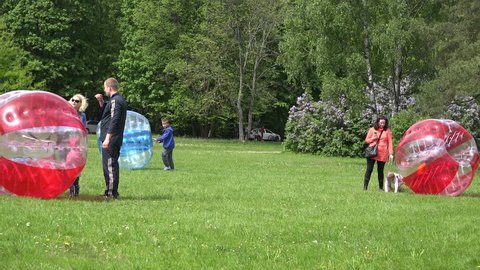 VILNIUS, LITHUANIA - MAY 23: Kids with parents spent leisure with zorb balls bubbles in park on May 23, 2015 in Vilnius, Lithuania. Active nontraditional recreation. Tracking follow panorama shot. 4K