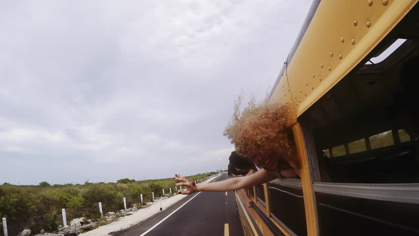 Friends hanging head out of bus window, enjoying