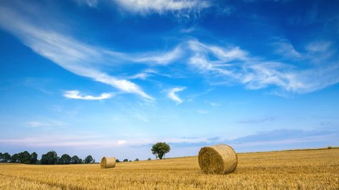 Stubble field with straw bales under blue sky with cirrus clouds. 4k timelapse 4096x2304