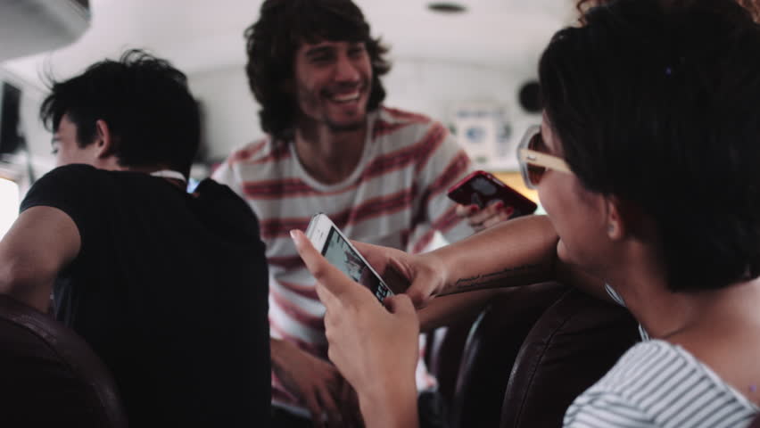 Male and female friends sitting and talking in bus, using mobile phone