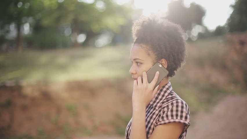 Attractive african american business woman commuter using smartphone walking in city at sunset