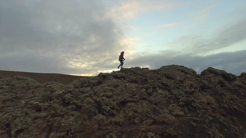 AERIAL: Young woman hiking up on the edge of volcanic crater in autumn evening