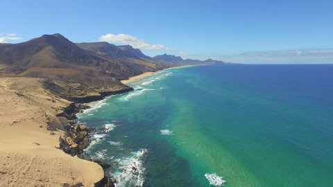 AERIAL: Amazing picturesque sandy beach with huge volcanoes and crystal clear emerald ocean, Cofete beach, Canary Islands
