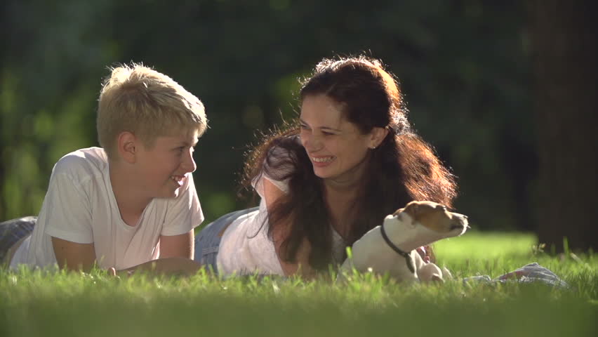 mom with teen son in the Park with a very cute puppy Jack Russell Terrier fun play ,feed him a treat and very happy, slow motion