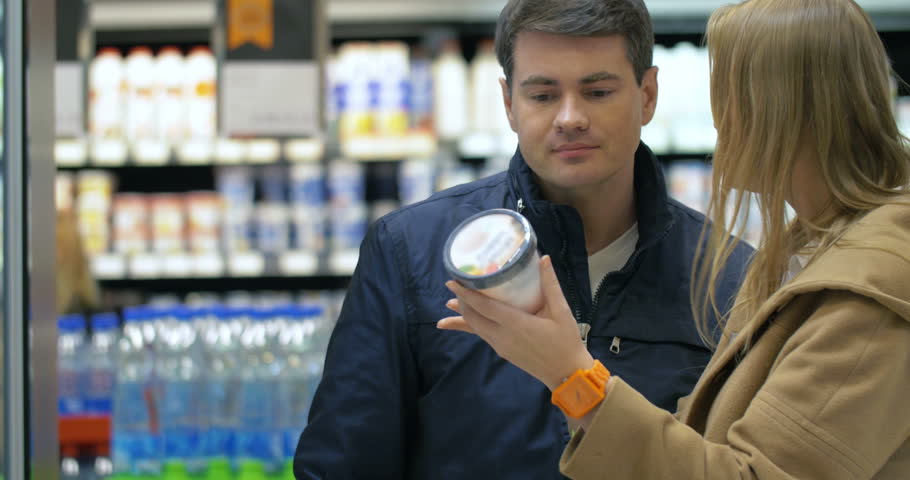 Young couple shopping in the supermarket. Man taking ice-cream from the fridge, but woman is angry with him. He putting it back, but returning alone and taking it again