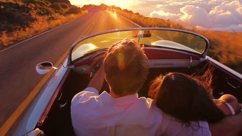 Happy Couple Driving on Country Road into the Sunset in Classic Vintage Sports Car. Steadicam Shot with Flare. Romantic Freedom Love Concept.