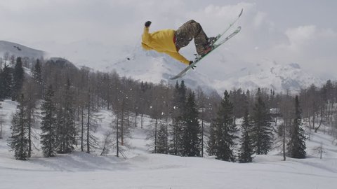 AERIAL SLOW MOTION: Freestyle skier jumping over big air kicker in sunny winter in ski resort Stock Video