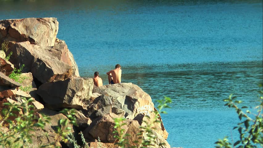 Two guys are sitting on a rock in front of the lake Individuals can not see