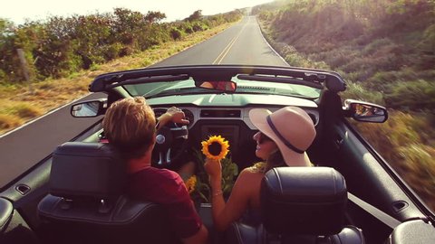 Happy Young Hipster Couple Driving Convertible on Country Road into Sunset. Romantic Freedom Vacation Concept. 20s-30s.