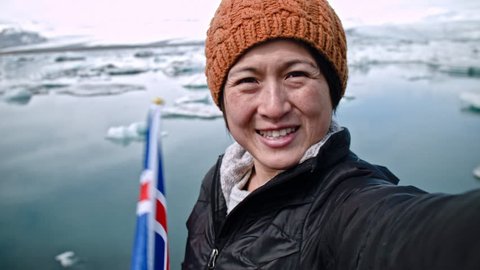 Asian chinese tourist taking selfie at glacier lagoon in iceland travel vacation fun with flag
