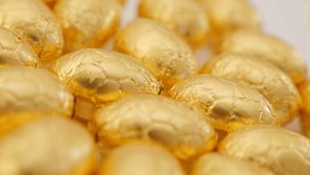 Golden foil wrapped Easter eggs on white surface slow pan 4K 2160p 30fps UltraHD footage - Traditional Easter chocolate eggs in gold foil 4K 3840X2160 UHD video