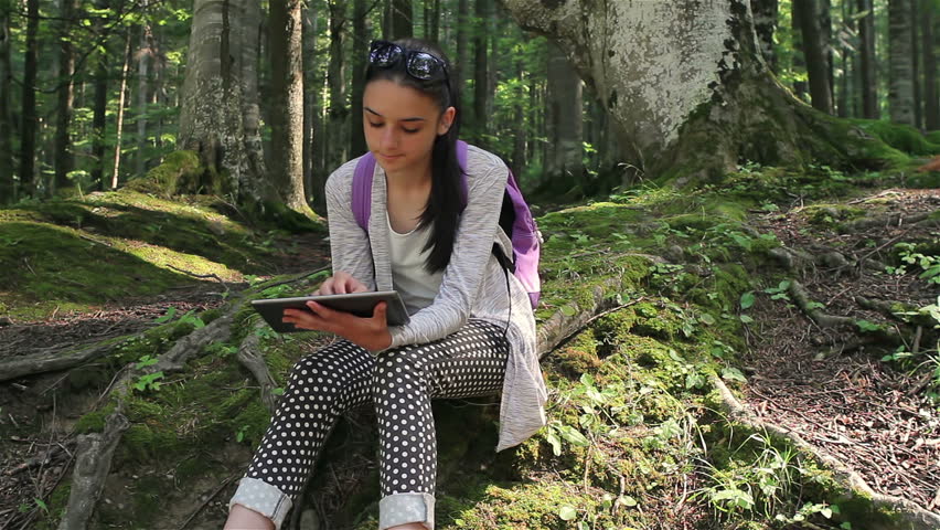 Teenage girl working on digital tablet pc in the forest.