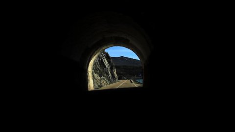 Traveling out of a Tunnel on Highway - Traveling front from car. Started in black within a curve of a road tunnel. After coming to light of a hilly landscape with river swamp
