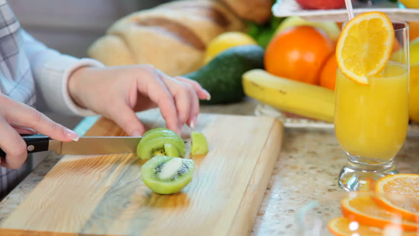 women hands preparing fruit salad slicing kiwi on chopping board