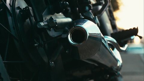 Close up left to right dolly sliding shot of a biker kickstarting the engine of a custom built cafe racer motorcycle 