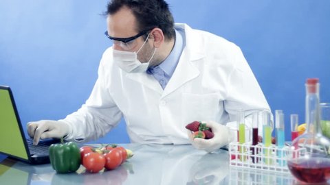 Male scientist in laboratory examining orange and writing results on laptop