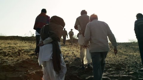 ANDHRA PRADESH, INDIA - CIRCA MAY 2013 - Traditional village elders walk up dry desert land, long shot, lens flare