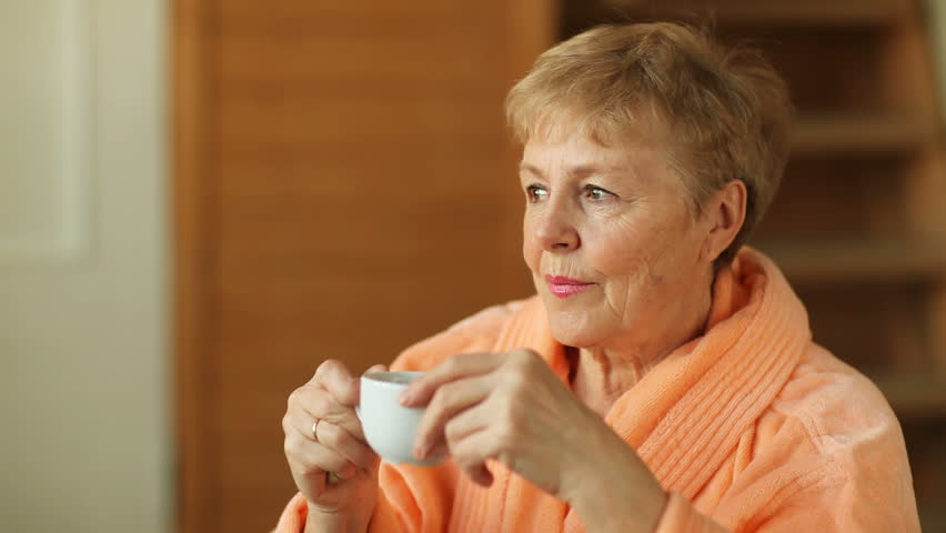 Thoughtful senior woman drinking coffee from white cup 