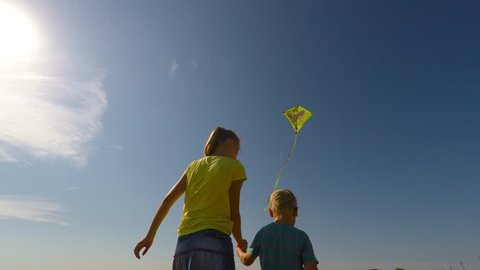 Older sister helping younger brother to play with a kite in the meadow.