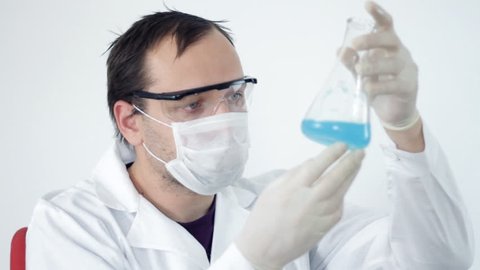 Male scientist examining Erlenmeyer flask with blue liquid