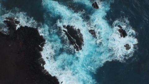 Spinning aerial of the ocean waves washing up on a black basalt rock in Hawaii.