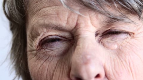 Close up of old woman with very wrinkled face squeezing her eyes from open to tight shut in an effort to see something.