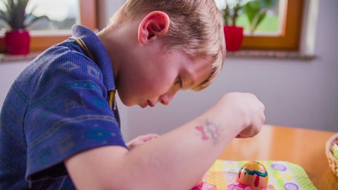 Carefully painting on egg in slow motion 4K. Side shot of young boy working with Easter eggs, painting decorations with special edible colors.