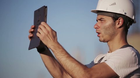 Engineer builder using tablet and walkie talkie, giving instructions at a construction site