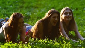 Three friends, young girls, having fun in park, laying on grass, relaxing, laughing, slow motion.