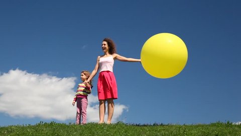 woman with daughter and yellow balloon stand on green grass meadow