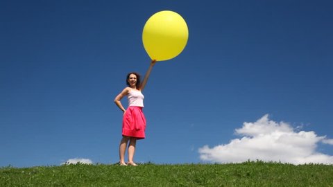 woman with yellow balloon stands on green grass meadow