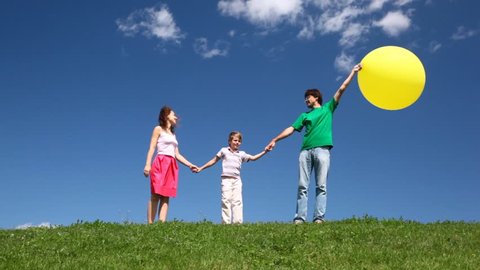 happy family of three with yellow balloon on hill with green grass and wildflowers 