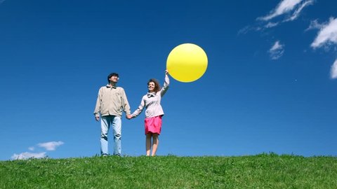 man and woman holding hands with yellow balloon walk on hill