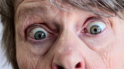 Close up of old woman's face looking down, then to camera; she gets startled and wide eyed and blinks rapidly.