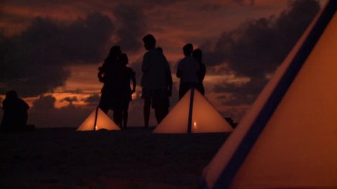 A zoom out shot of tents placed on the beach and candles litted inside,Maldives
