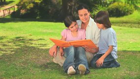 Mother looking at an album with her children while sitting on the grass oif a park