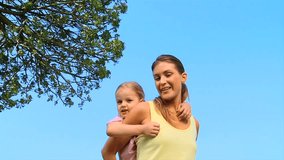 Woman giving a piggy back to her cute daughter outdoors